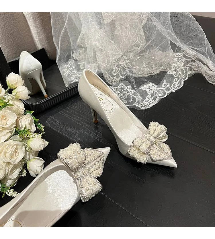 White satin stiletto high heels with pointed toe, pearl bow detail, by LYNHURD for brides and special occasions.