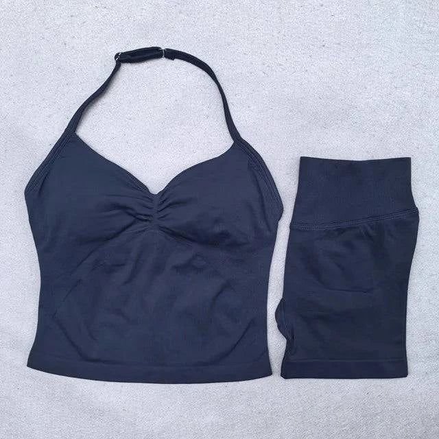 LYNHURD! women's backless halter top and high waist seamless shorts yoga set in a fitness pose against a gym background.